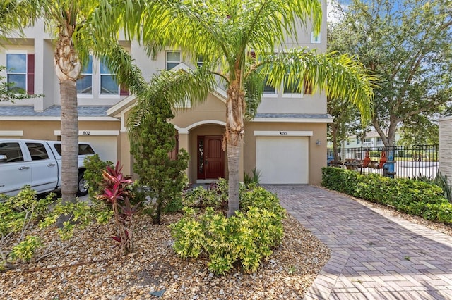 multi unit property with a garage, stucco siding, fence, and decorative driveway