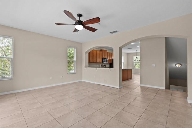 unfurnished living room with light tile patterned flooring, plenty of natural light, a ceiling fan, and baseboards