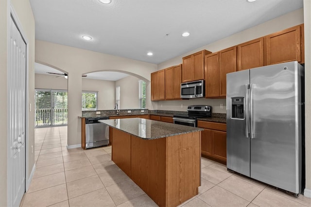 kitchen featuring stainless steel appliances, arched walkways, a center island, brown cabinets, and light tile patterned floors