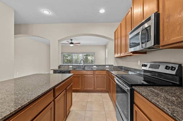 kitchen with appliances with stainless steel finishes, arched walkways, a sink, brown cabinets, and ceiling fan