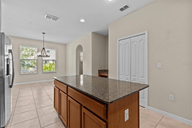 kitchen featuring stainless steel refrigerator with ice dispenser, light tile patterned floors, a center island, brown cabinetry, and arched walkways