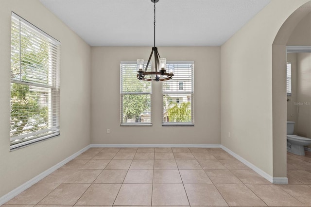 unfurnished dining area featuring light tile patterned flooring, arched walkways, a chandelier, and baseboards