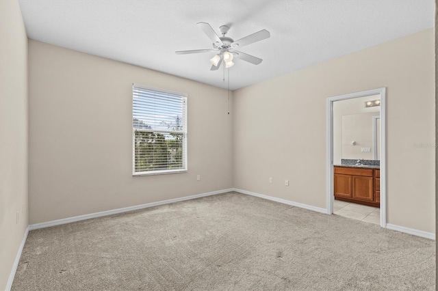 unfurnished bedroom featuring light carpet, baseboards, connected bathroom, and ceiling fan