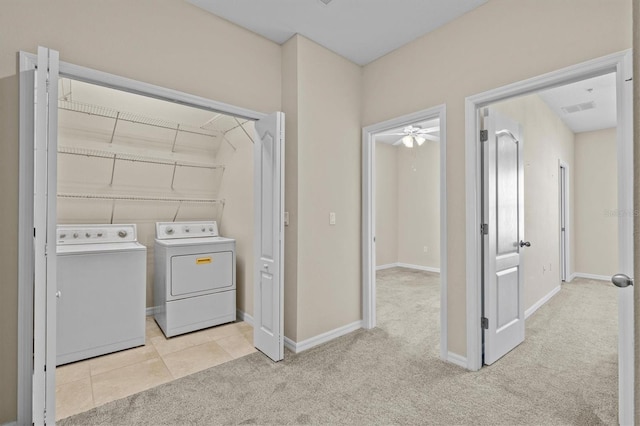 laundry area with washing machine and clothes dryer, light colored carpet, a ceiling fan, and baseboards