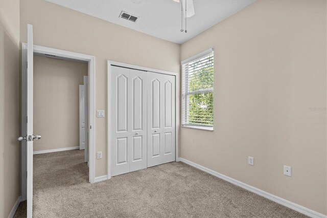 unfurnished bedroom with light colored carpet, a closet, baseboards, and a ceiling fan