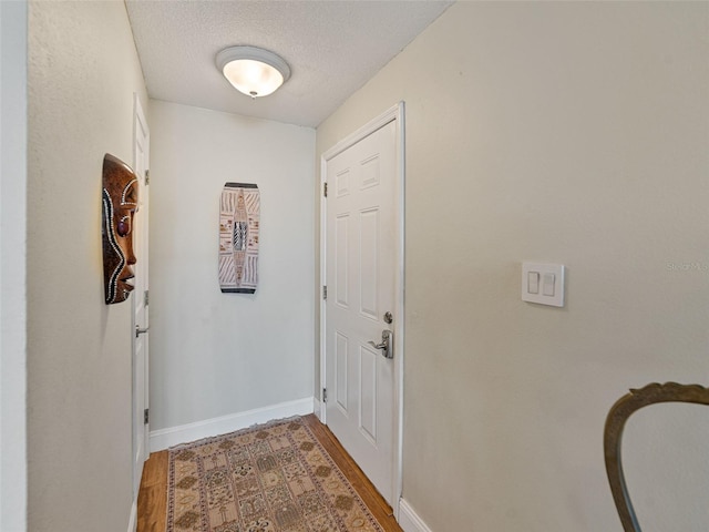 hall with baseboards, a textured ceiling, and wood finished floors