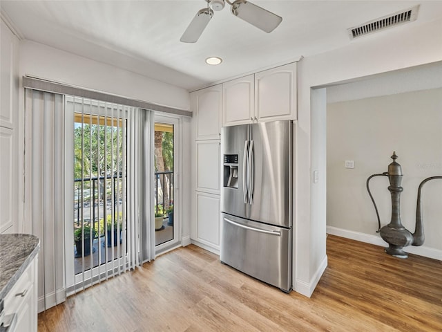 kitchen with stainless steel refrigerator with ice dispenser, visible vents, baseboards, white cabinets, and light wood-style floors