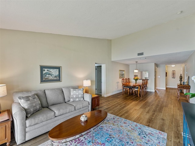 living area with baseboards, wood finished floors, visible vents, and high vaulted ceiling