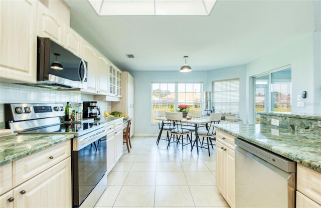 kitchen with stainless steel appliances, glass insert cabinets, light stone counters, light tile patterned floors, and baseboards