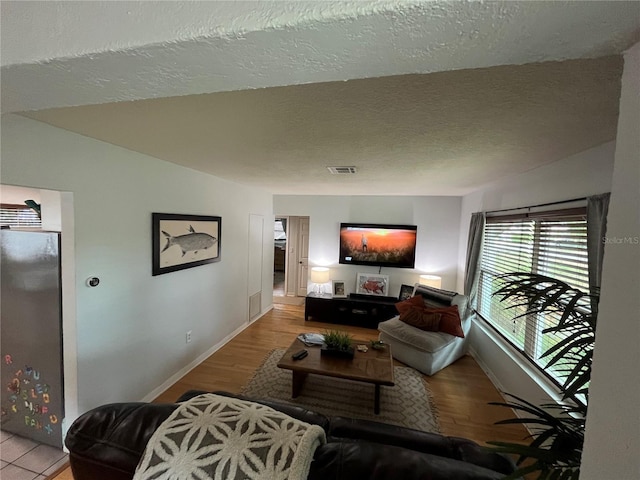 living room featuring baseboards, a textured ceiling, wood finished floors, and visible vents