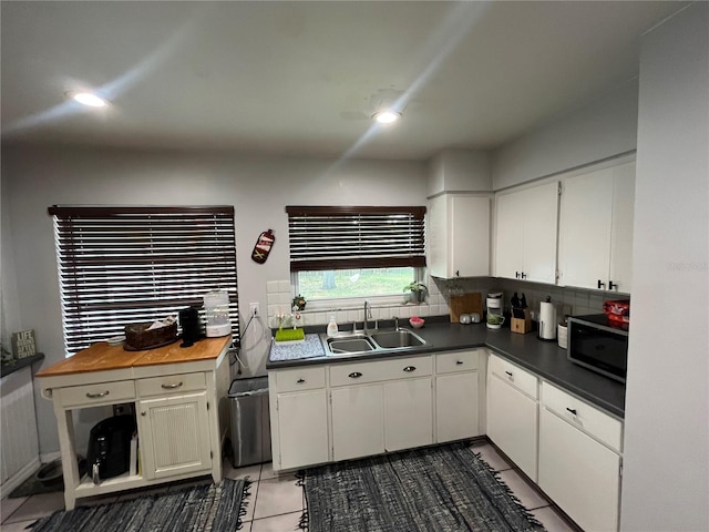kitchen featuring dark countertops, white cabinetry, stainless steel microwave, tasteful backsplash, and a sink