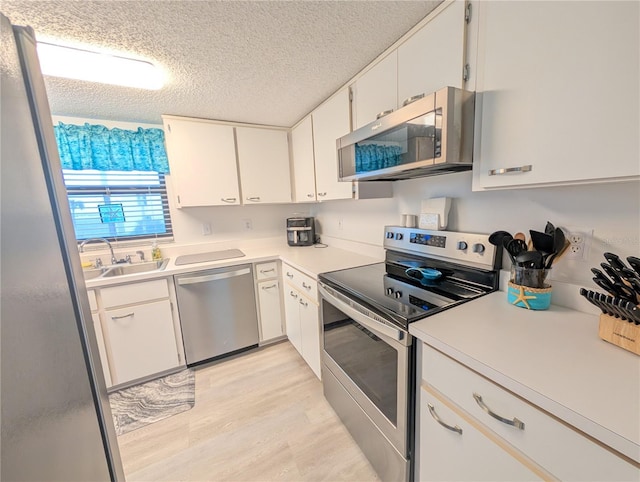 3100 Ocean Shore Blvd Unit 101, Ormond Beach, FL 32176 - kitchen featuring stainless steel appliances, a sink, a textured ceiling, light wood-style flooring, and white cabinetry