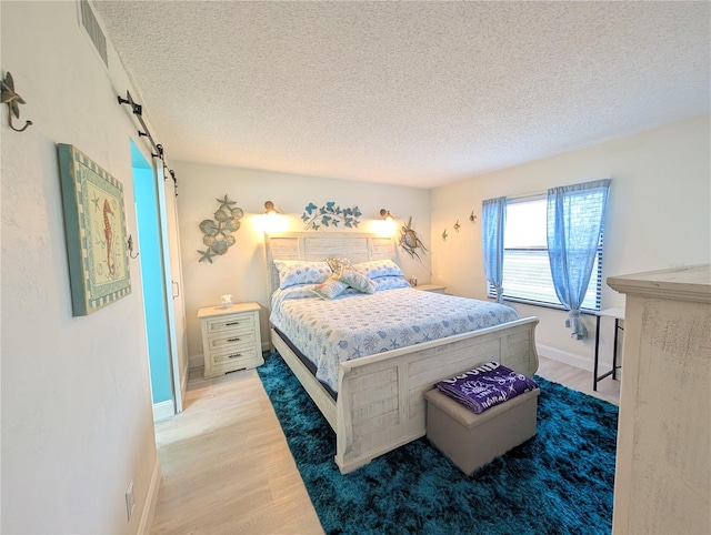 3100 Ocean Shore Blvd Unit 101, Ormond Beach, FL 32176 - bedroom featuring a barn door, light wood finished floors, a textured ceiling, and baseboards