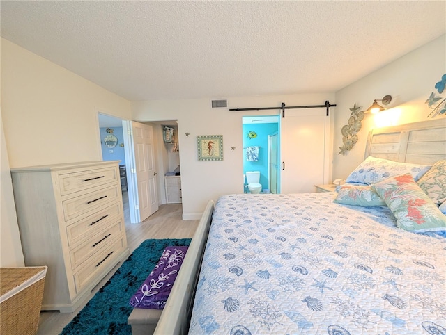 3100 Ocean Shore Blvd Unit 101, Ormond Beach, FL 32176 - bedroom with light wood-style flooring, a barn door, a textured ceiling, and baseboards