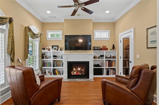 sitting room with a ceiling fan, wood finished floors, a fireplace with flush hearth, crown molding, and recessed lighting