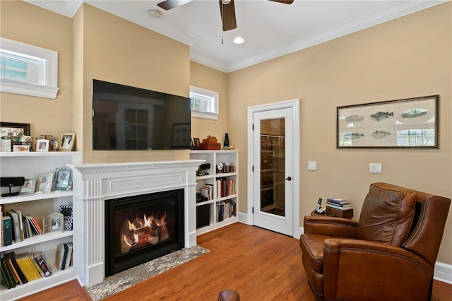sitting room featuring wood finished floors, crown molding, a ceiling fan, a fireplace with flush hearth, and baseboards