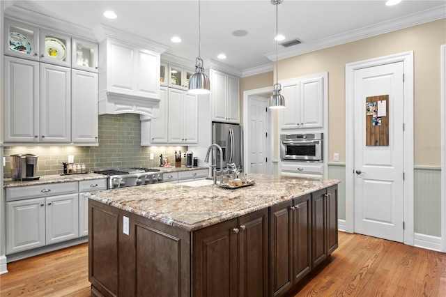 kitchen with a sink, stainless steel appliances, light wood finished floors, white cabinetry, and ornamental molding