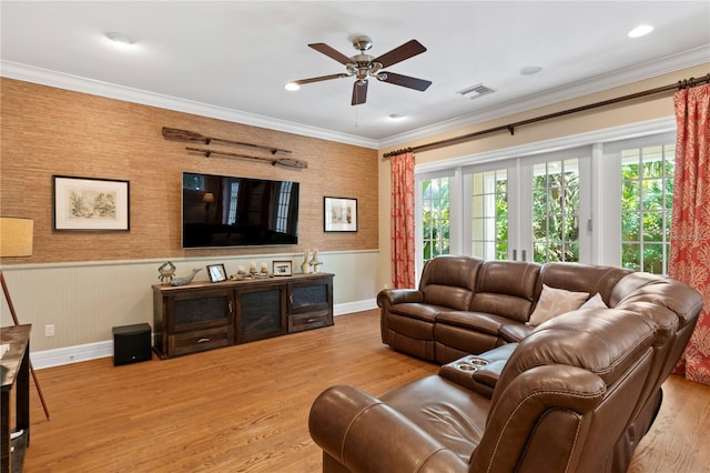 living area featuring ceiling fan, a wainscoted wall, wood finished floors, crown molding, and baseboards