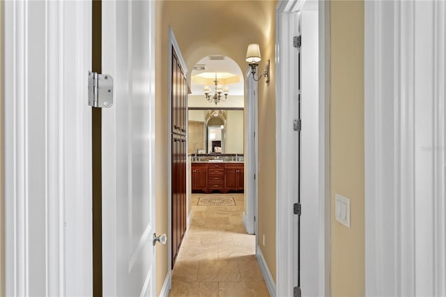 hallway featuring a chandelier and baseboards