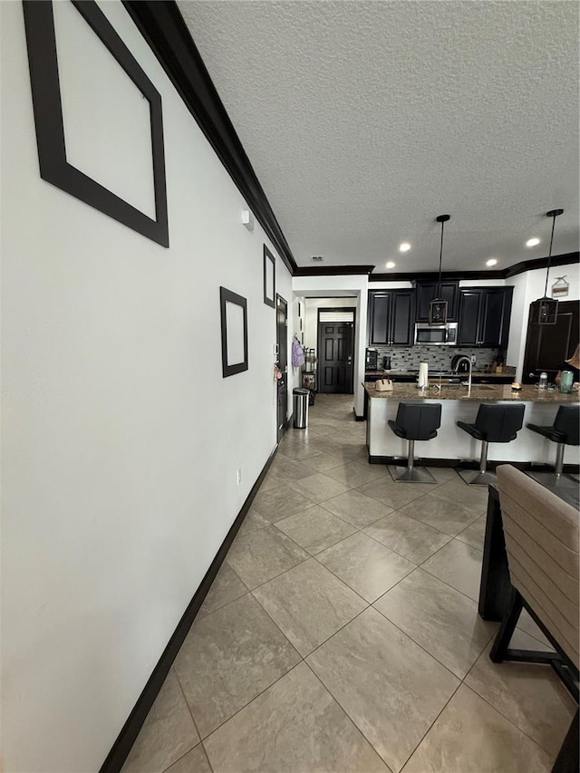 hallway featuring a textured ceiling, crown molding, baseboards, recessed lighting, and light tile patterned flooring