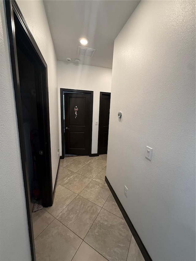 corridor with baseboards, visible vents, and light tile patterned floors