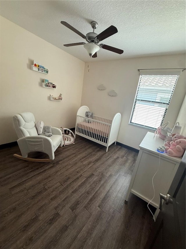 bedroom featuring a nursery area, ceiling fan, a textured ceiling, and dark wood-type flooring