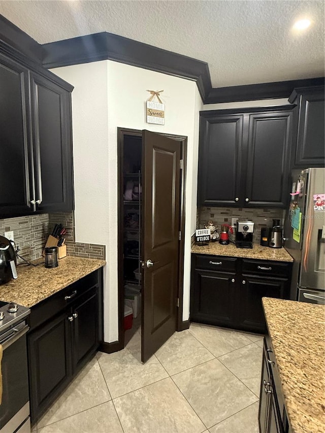 kitchen featuring dark cabinets, decorative backsplash, a textured ceiling, and appliances with stainless steel finishes