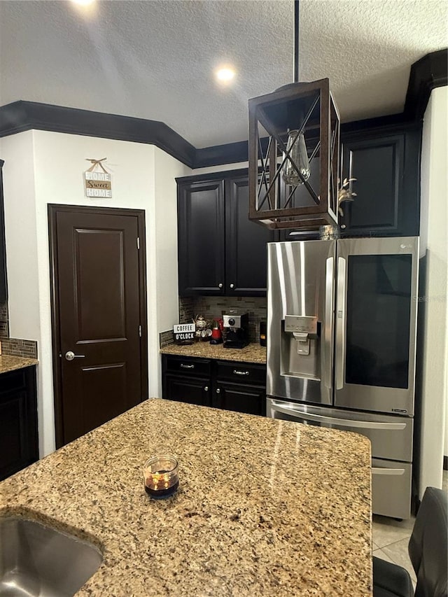 kitchen featuring a textured ceiling, light stone counters, stainless steel fridge with ice dispenser, and tasteful backsplash