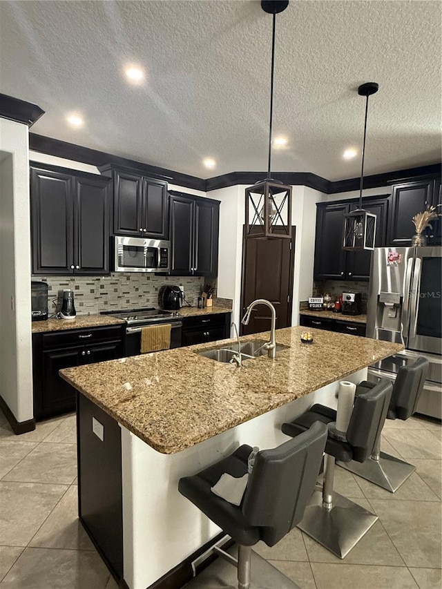 kitchen with light stone counters, a breakfast bar area, dark cabinets, a sink, and appliances with stainless steel finishes