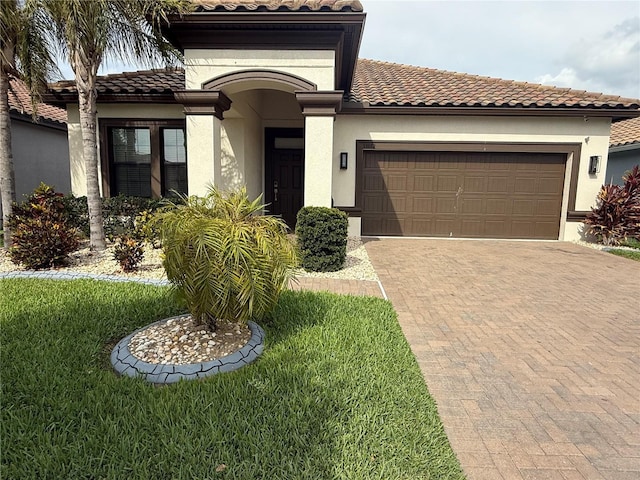 mediterranean / spanish-style home with a front lawn, decorative driveway, stucco siding, a tiled roof, and an attached garage