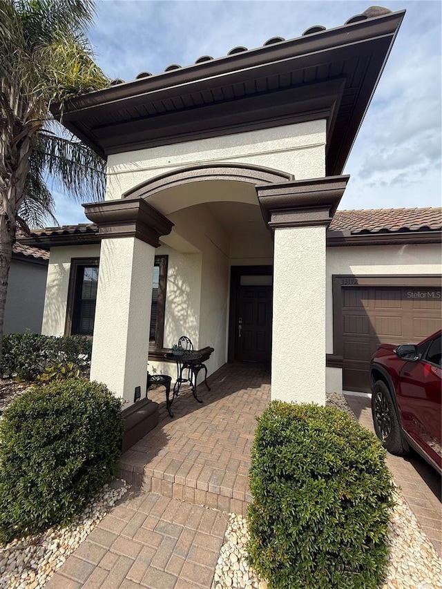 view of exterior entry with a tiled roof, an attached garage, and stucco siding