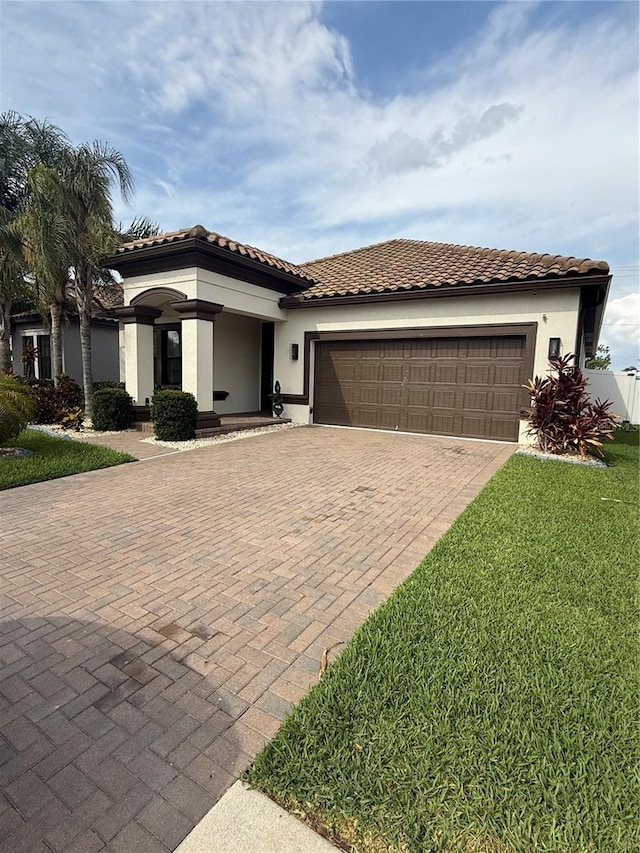 mediterranean / spanish-style home with a front lawn, a tile roof, a garage, stucco siding, and decorative driveway