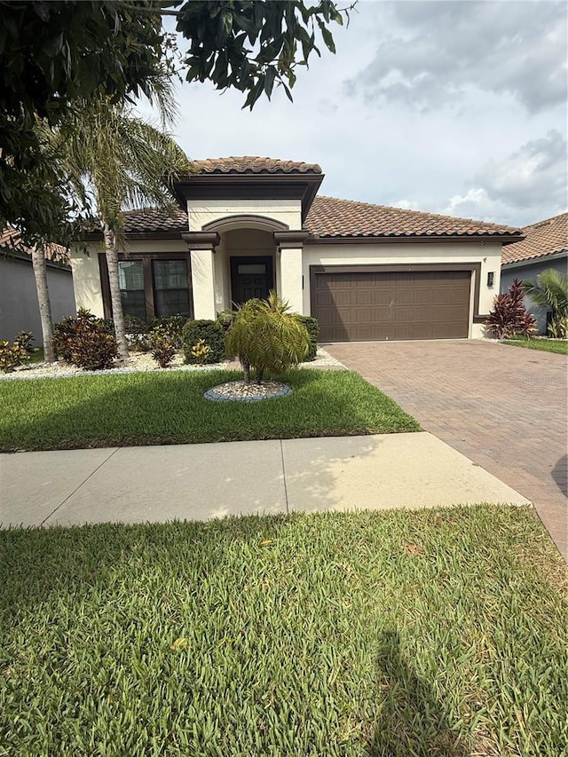mediterranean / spanish-style house with a tiled roof, a garage, decorative driveway, a front lawn, and stucco siding