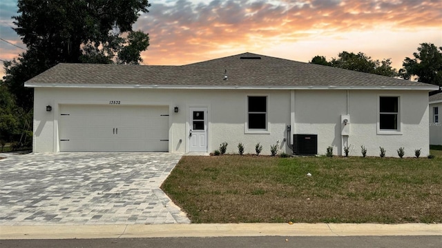 view of front of home featuring roof with shingles, an attached garage, stucco siding, a front lawn, and decorative driveway