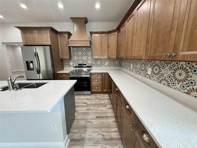 kitchen with appliances with stainless steel finishes, recessed lighting, a sink, premium range hood, and light wood-type flooring