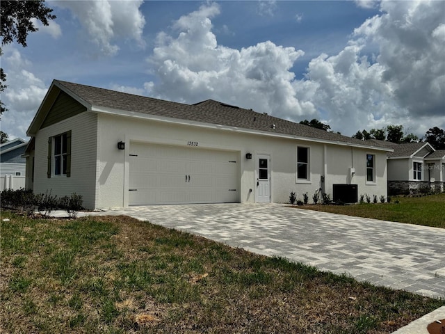 view of front facade featuring an attached garage, stucco siding, cooling unit, and decorative driveway