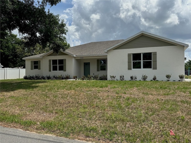 ranch-style house featuring a front yard, roof with shingles, and fence
