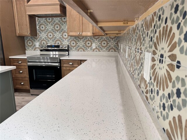 kitchen featuring custom exhaust hood, electric stove, backsplash, brown cabinets, and light countertops
