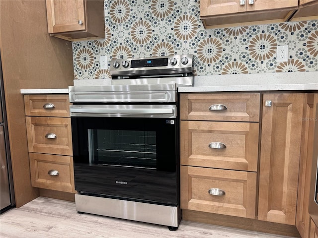 kitchen featuring light wood finished floors, light countertops, tasteful backsplash, and electric stove