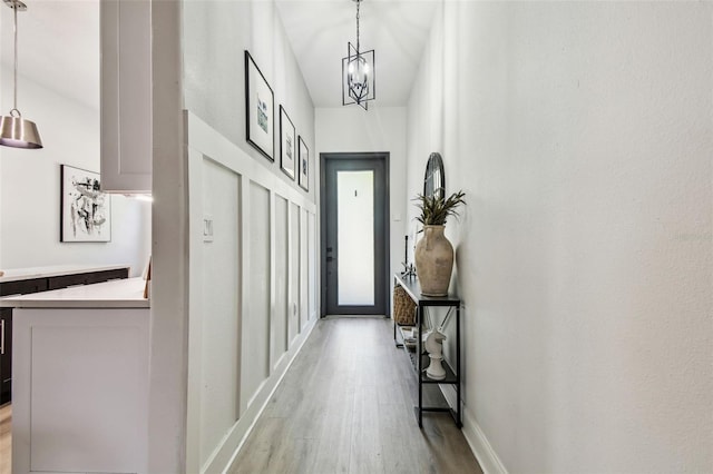 doorway to outside featuring baseboards, light wood-style flooring, and an inviting chandelier