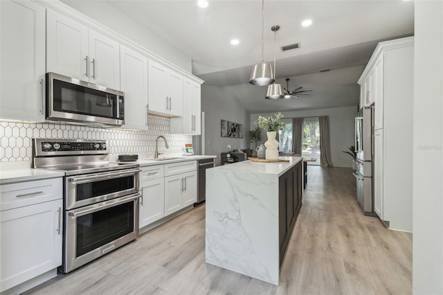 kitchen featuring appliances with stainless steel finishes, a sink, white cabinetry, decorative backsplash, and a kitchen island