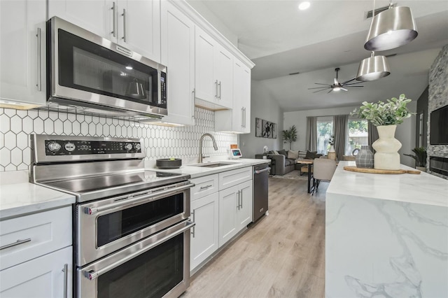 kitchen featuring decorative backsplash, appliances with stainless steel finishes, a sink, open floor plan, and light wood-style floors