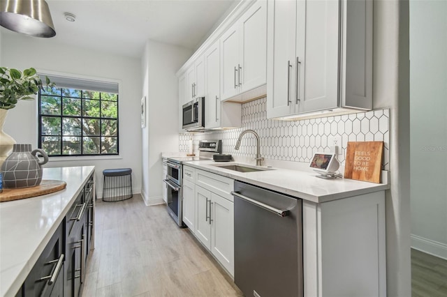 kitchen with decorative backsplash, light wood-style floors, light countertops, a sink, and appliances with stainless steel finishes