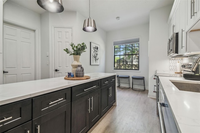 kitchen with white cabinets, hanging light fixtures, dark cabinets, stainless steel microwave, and light wood-type flooring