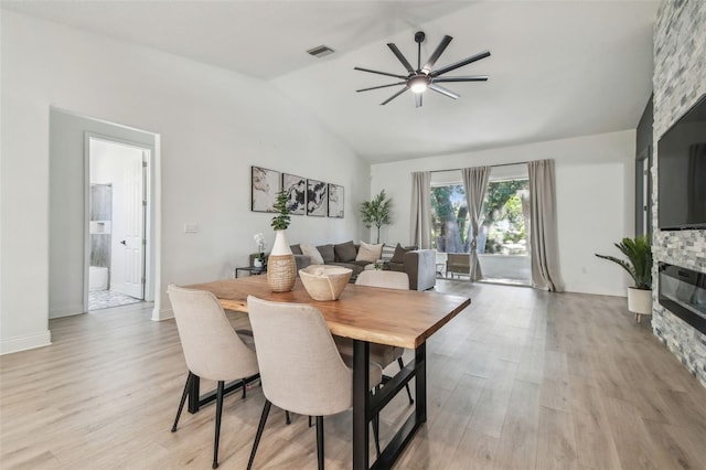 dining area with a fireplace, light wood-style floors, a ceiling fan, lofted ceiling, and visible vents