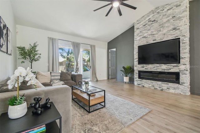 living area featuring a stone fireplace, a ceiling fan, baseboards, wood finished floors, and vaulted ceiling
