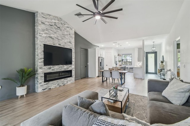 living area with a stone fireplace, a ceiling fan, high vaulted ceiling, and light wood-type flooring