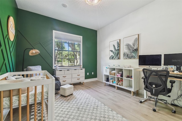 bedroom featuring a nursery area, baseboards, and wood finished floors