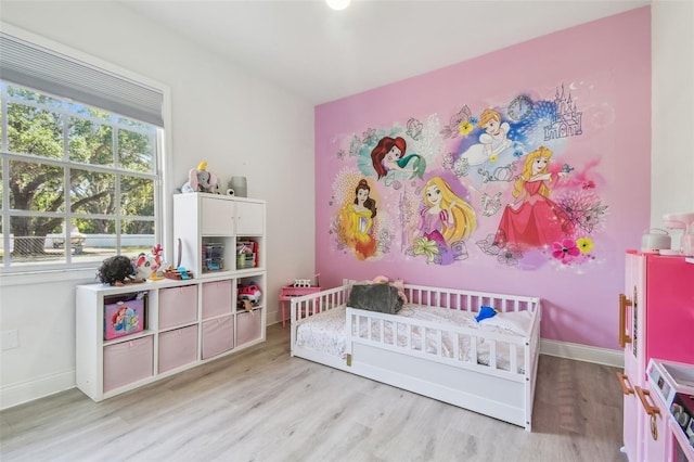 bedroom with light wood-type flooring, baseboards, and a crib