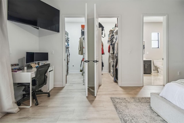 bedroom with a walk in closet, baseboards, a closet, and light wood-type flooring